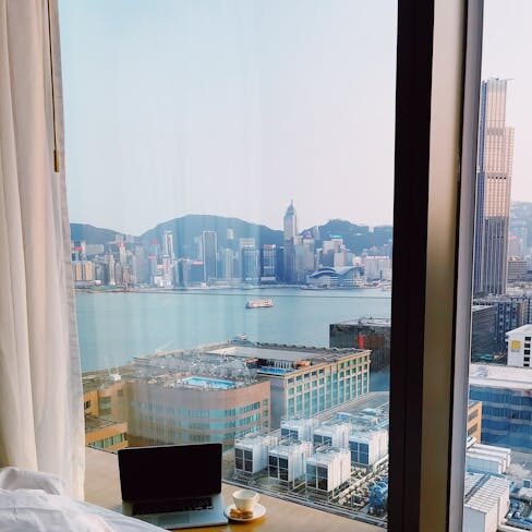 Cozy hotel room with cityscape view from bed, featuring a laptop and coffee by the window.